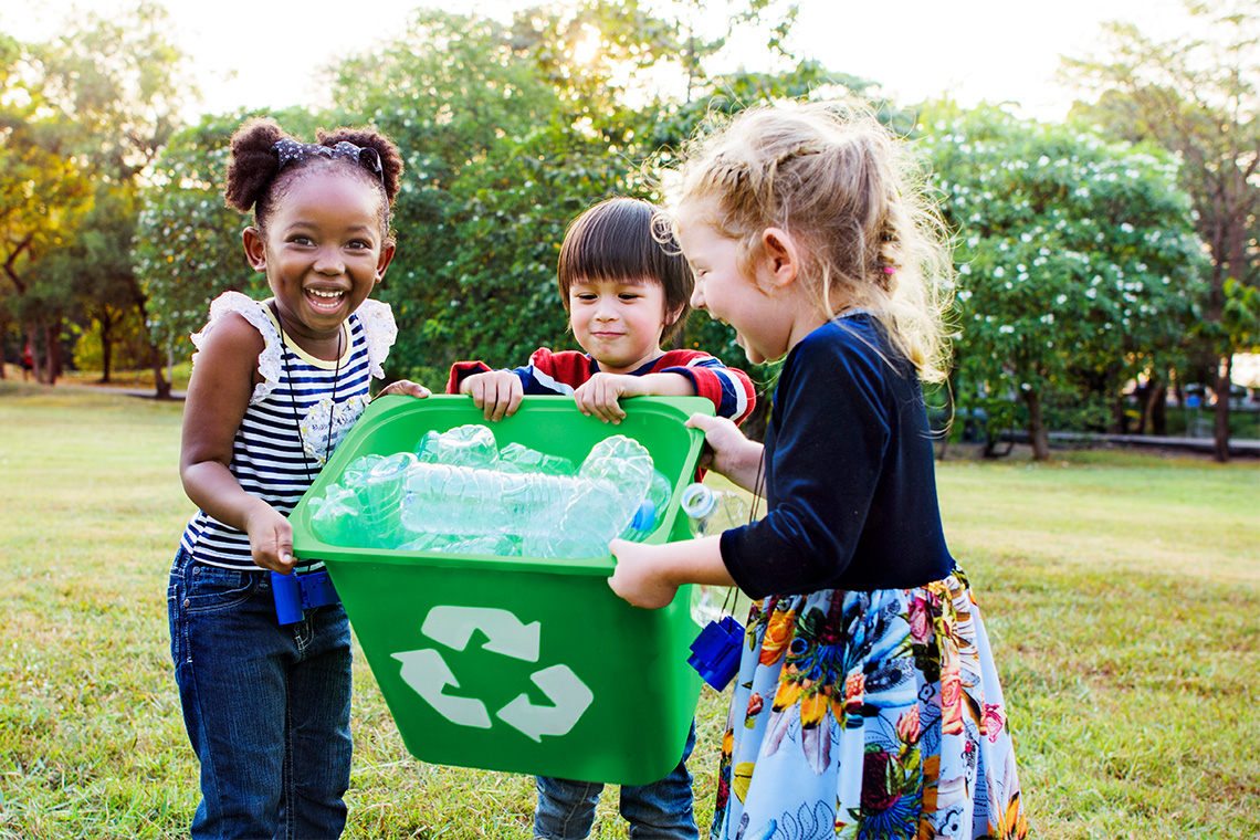 Three learners outside holding a recycling bin together.